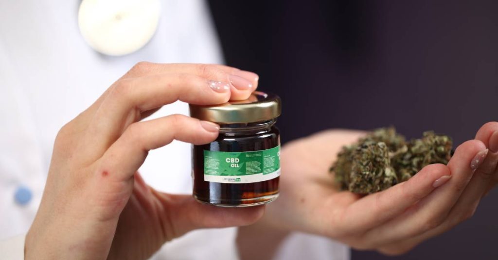A close-up of someone holding CBD oil in one hand and cannabis buds in the other. The CBD oil is dark.