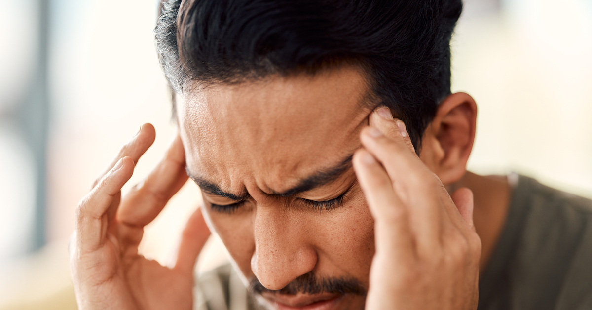 A man is holding his head in pain and has his eyes closed. He is having a bad headache and is in distress.