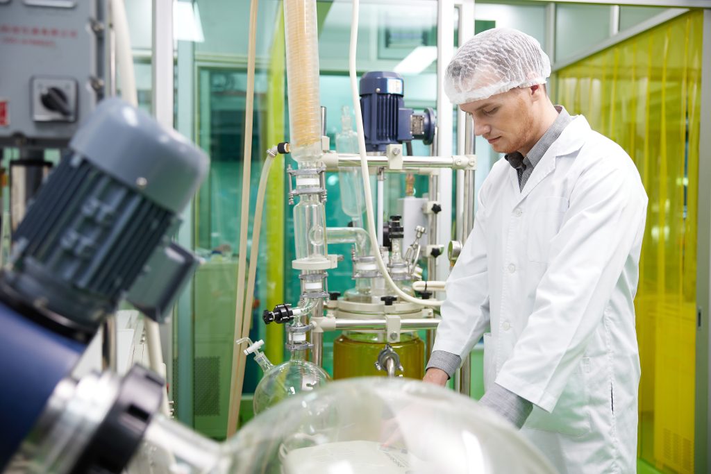 A scientist wearing protective gear near cannabis lab equipment. He's looking down and operating a machine.